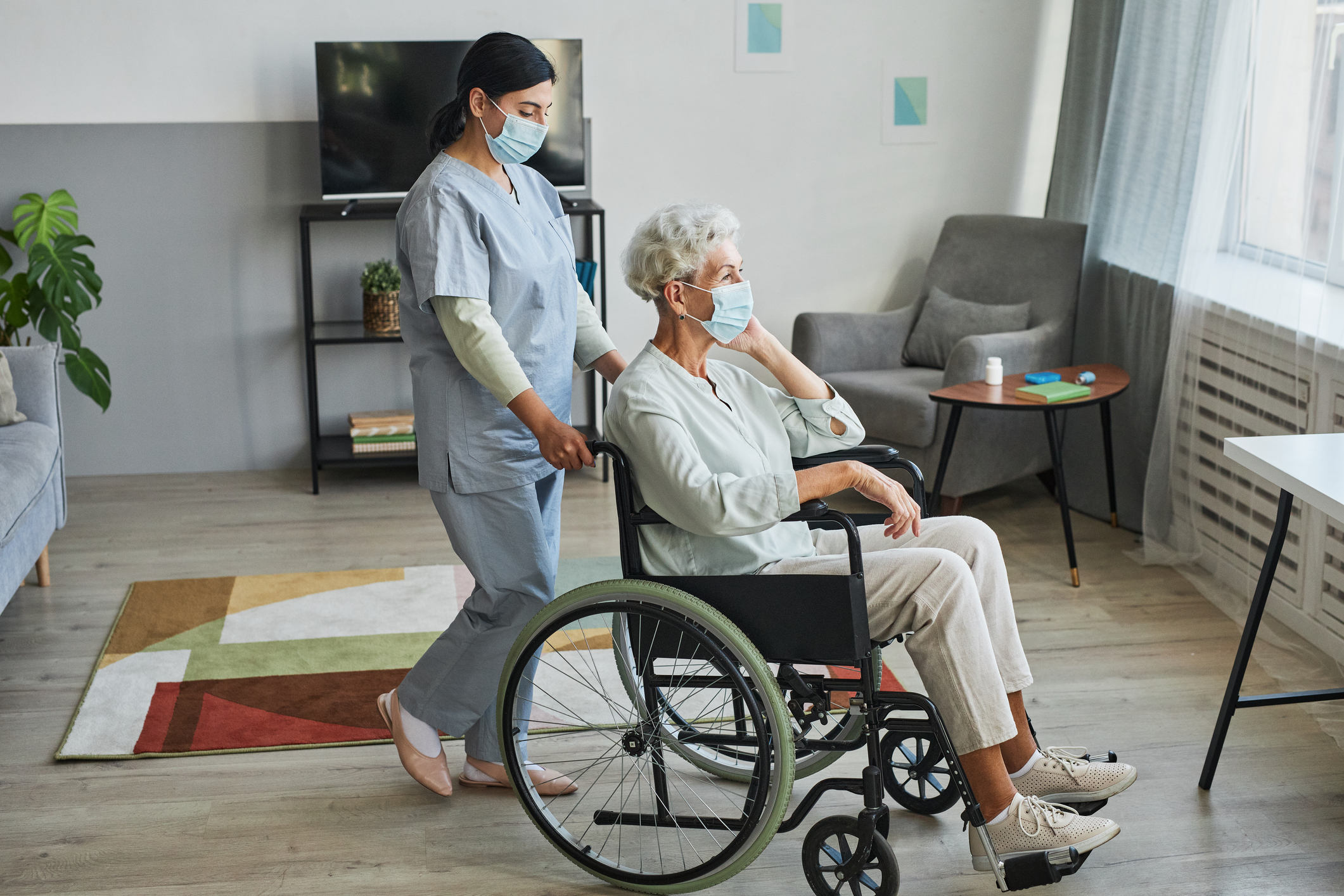 Elderly female on a wheel chair being pushed by  young female  carer in room